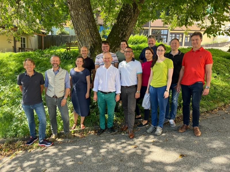 Gruppe von Menschen vor einem Baum und einer Wiese, Sonne scheint