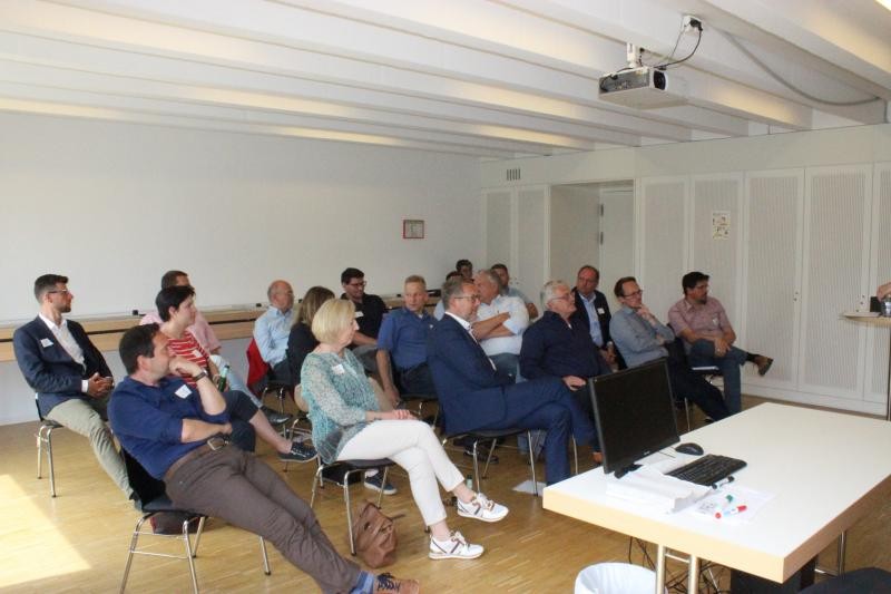 Gruppe von Menschen in einem Saal mit Tisch und Referent